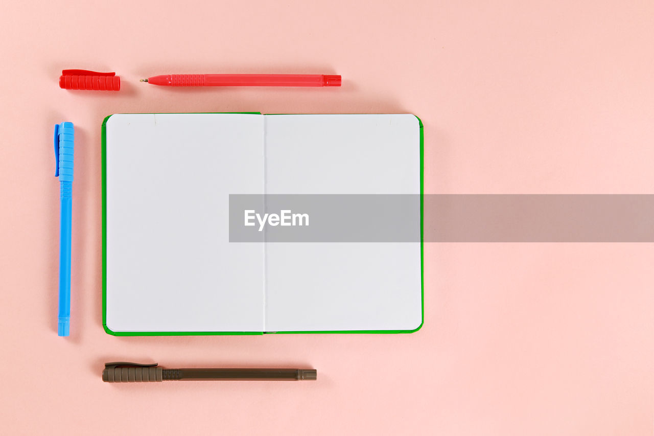 Directly above shot of diary and pens on pink background