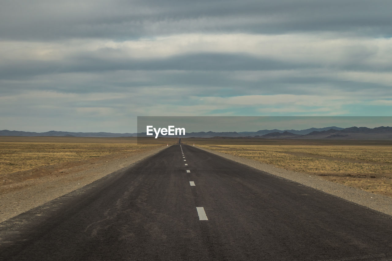 Road passing through landscape against cloudy sky