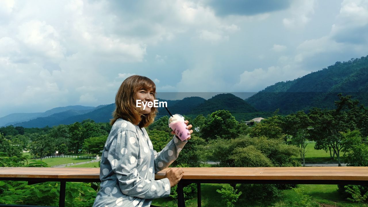 Woman holding drink against mountains