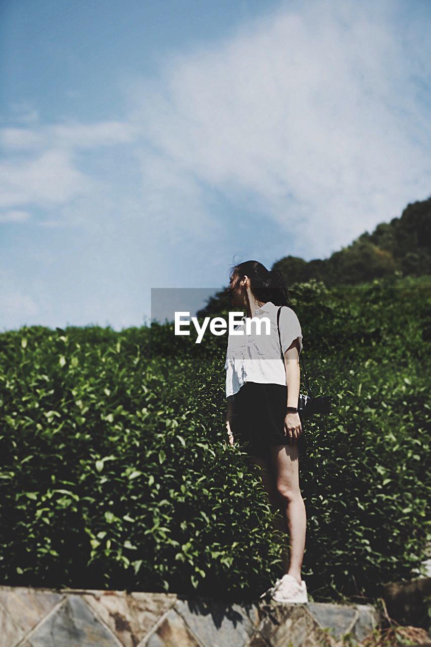 Low angle view of woman standing amidst plants on field against sky