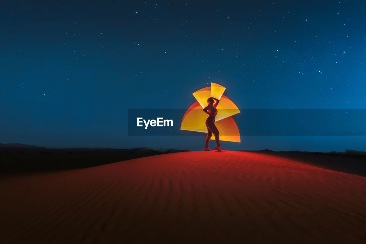 Full length of woman standing on sand dune against sky at night