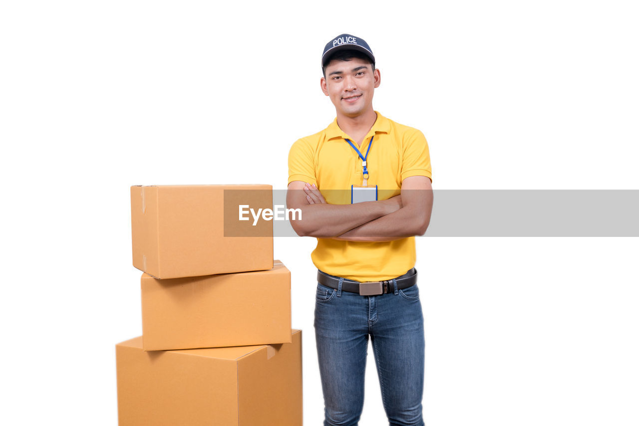 Portrait of smiling delivery man standing by packages against beige background