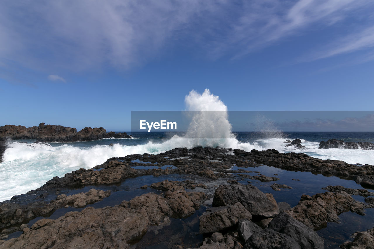 SCENIC VIEW OF WAVES SPLASHING ON ROCKS AGAINST SKY