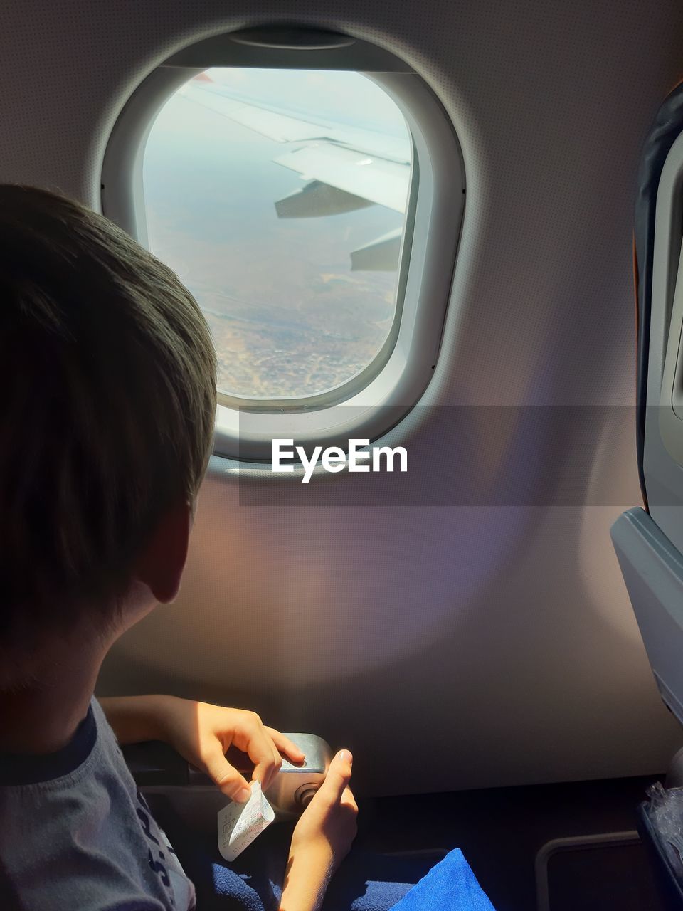 Boy looking through window while traveling in airplane