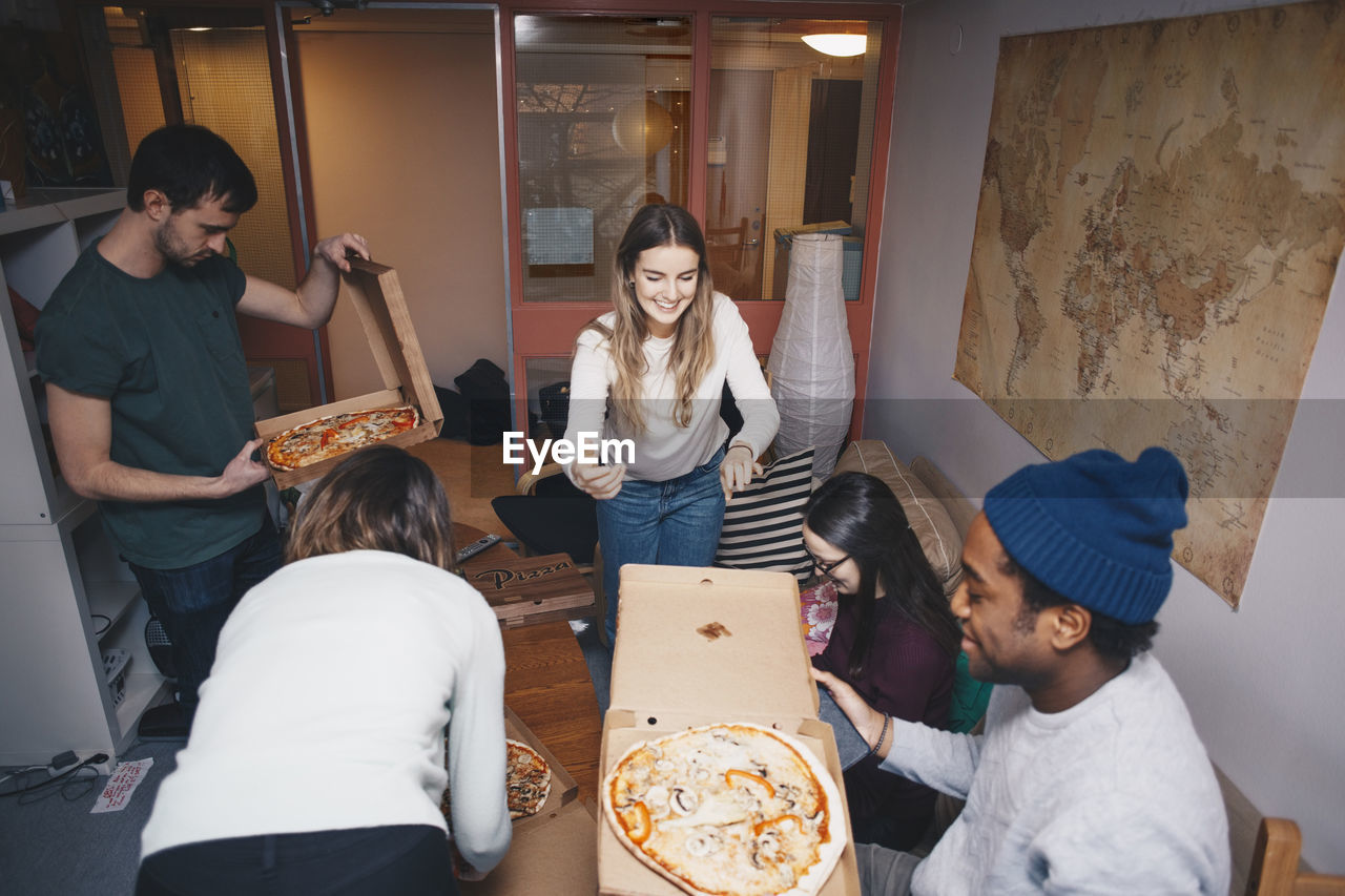 High angle view of young friends enjoying pizza party in dorm room