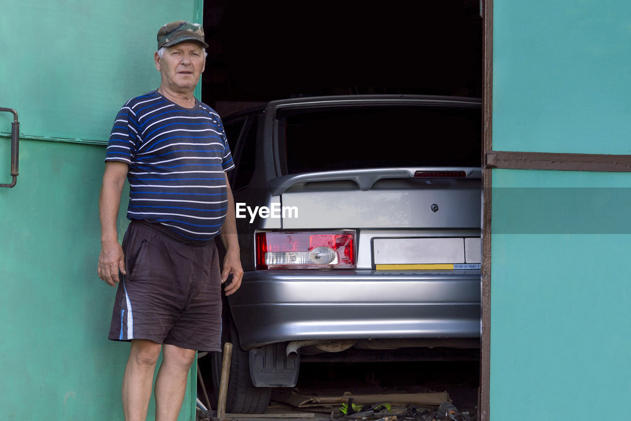 Old man grandfather in stands near garage. sunny autumn day. front view.