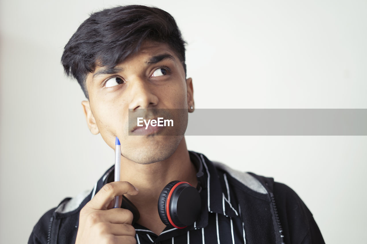 Portrait of asian young man good grooming holding pen looking sideways with doubtful expression.