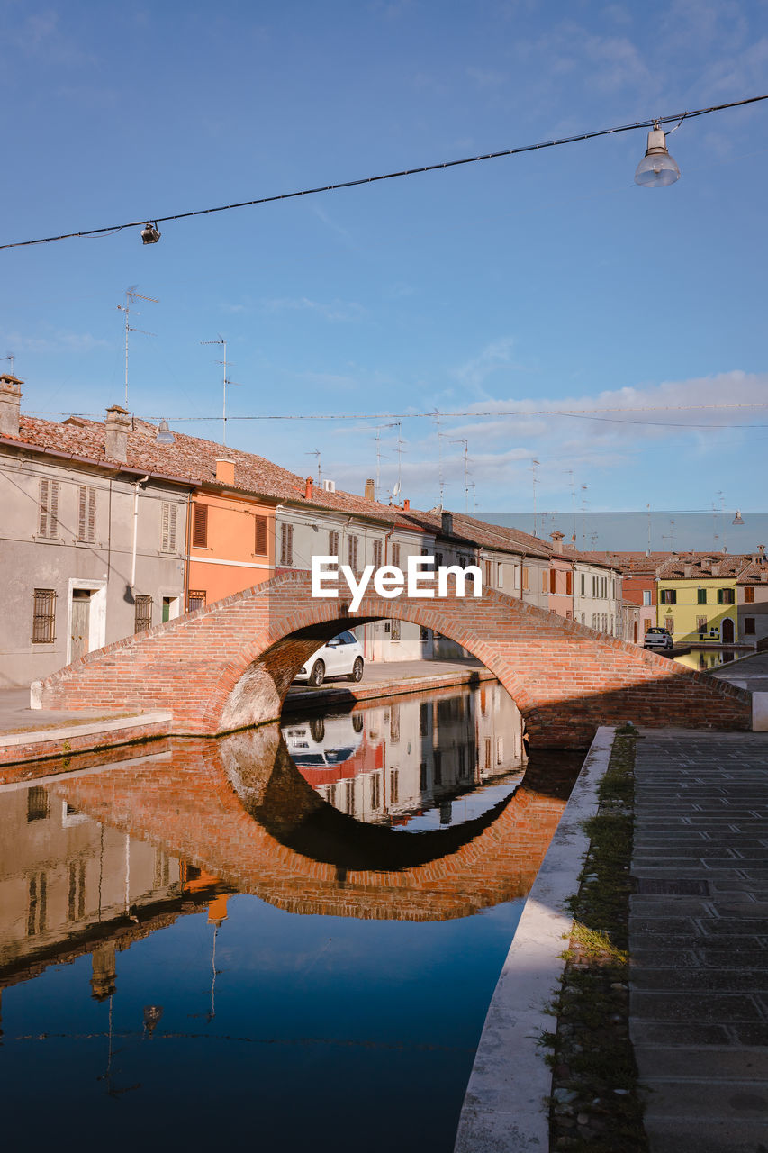 Bridge over canal by buildings against sky