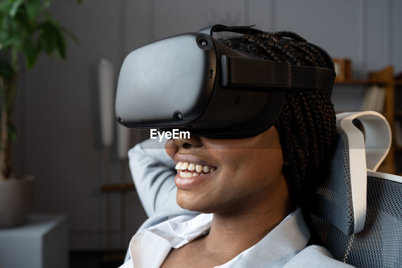 Happy relaxed afro woman in vr googles using virtual reality to relax and reduce stress at workplace