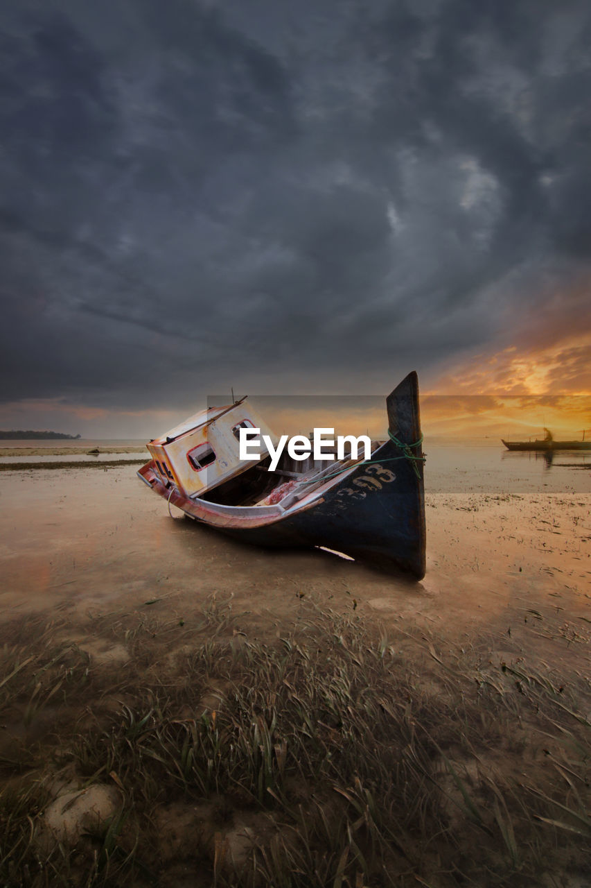 Abandoned ship on beach against sky during sunset