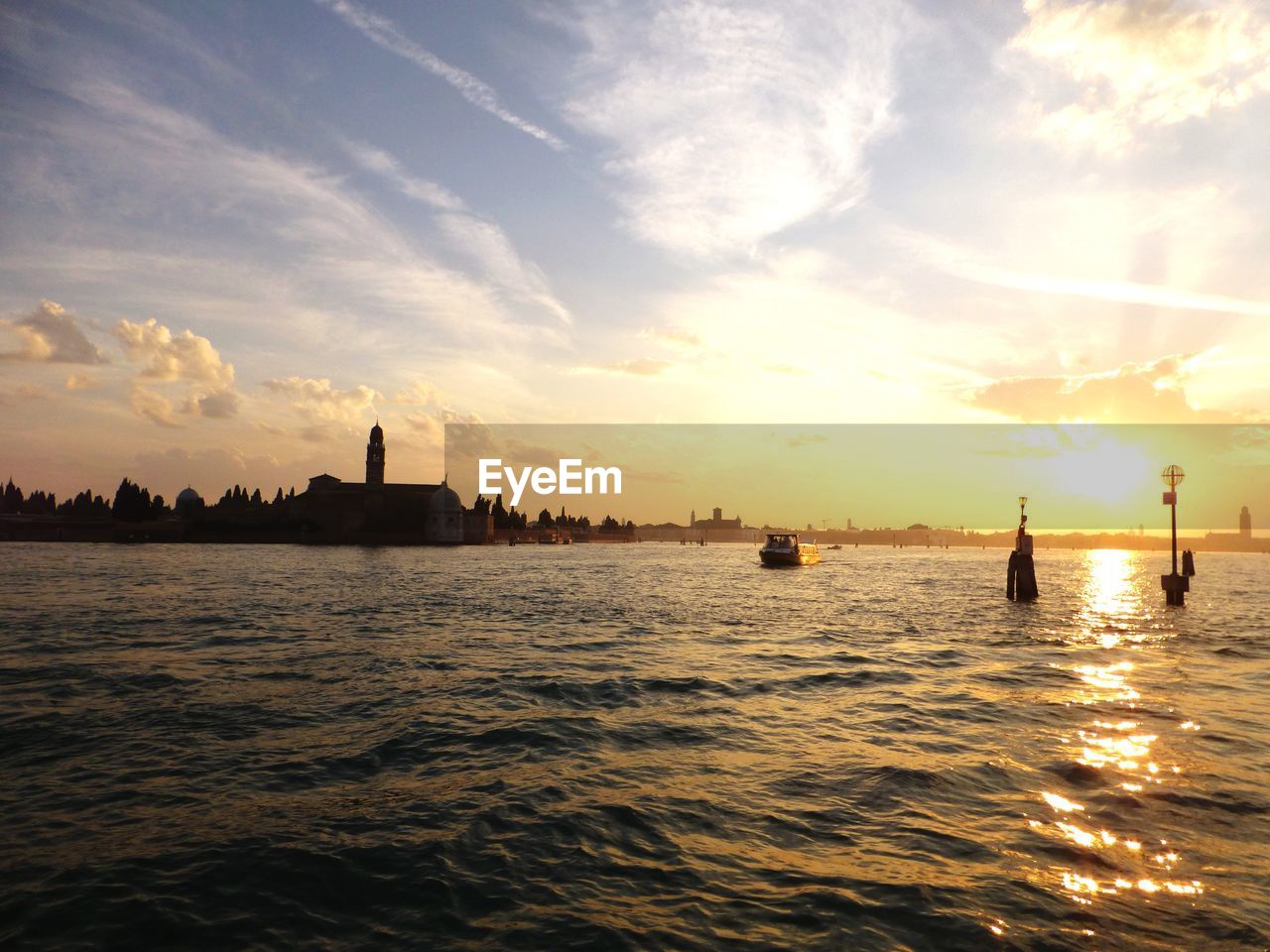 SILHOUETTE OF WOODEN POSTS IN SEA AGAINST SKY DURING SUNSET