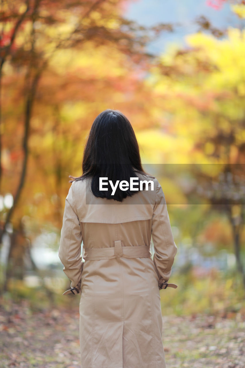 Rear view of woman standing against trees during autumn