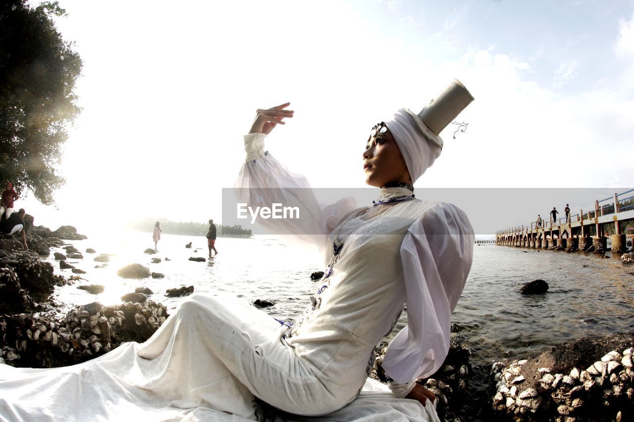Side view of woman wearing traditional clothing sitting against sea