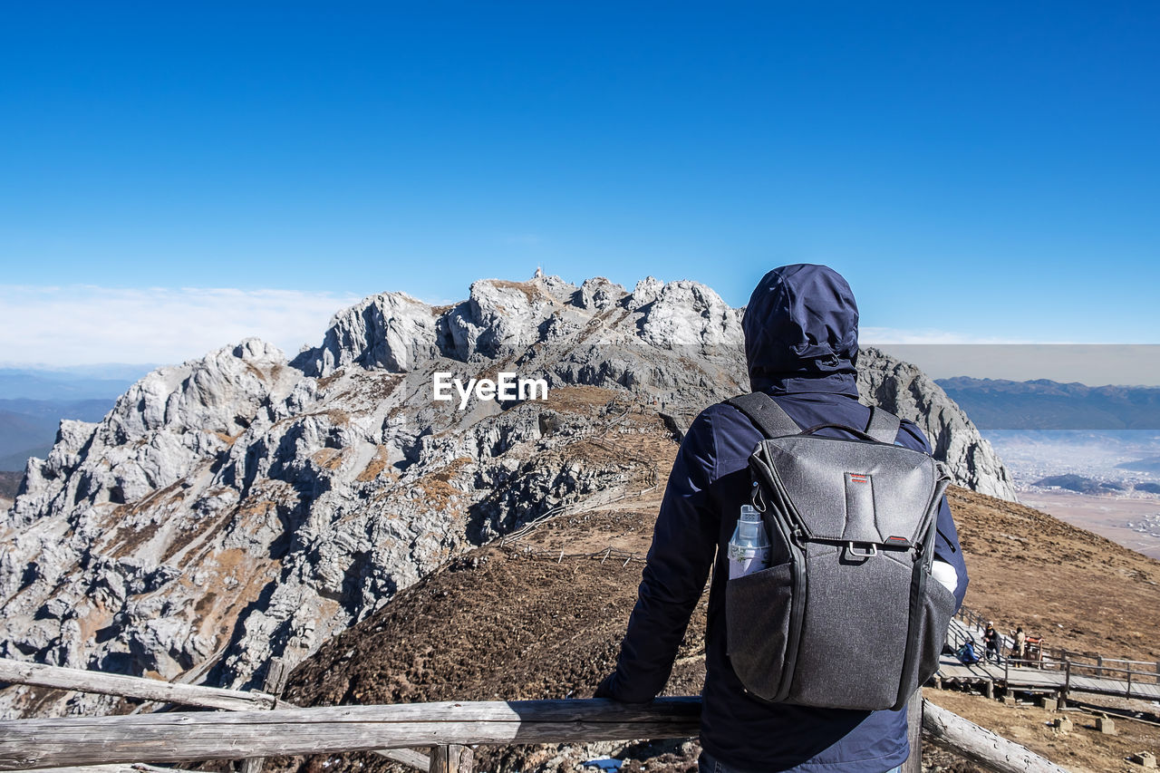 REAR VIEW OF PERSON ON ROCK AGAINST SKY