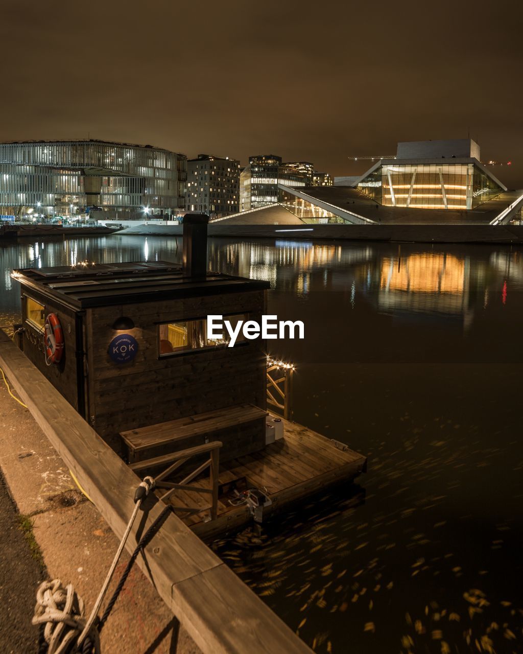 Illuminated bridge over river by buildings against sky at night