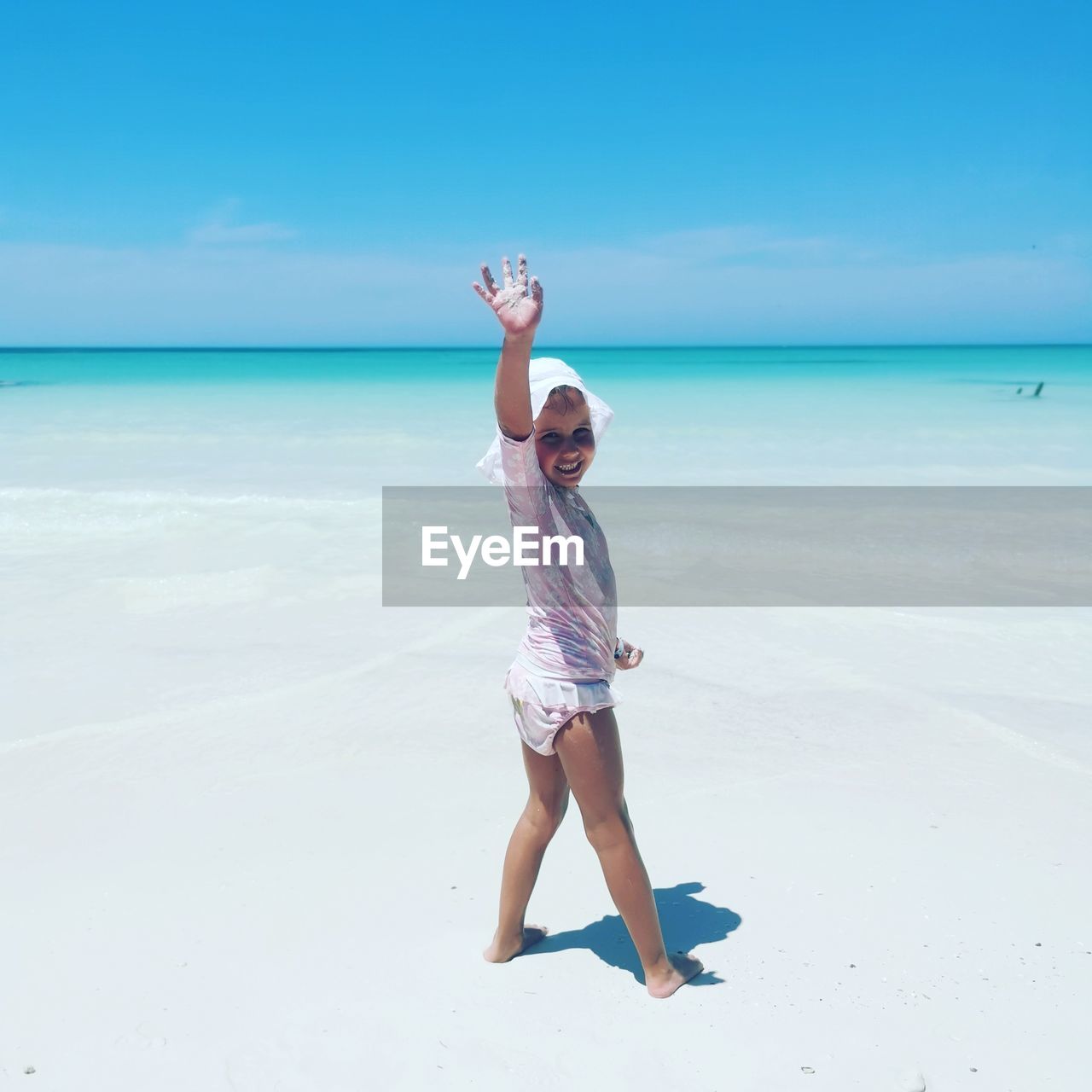 Full length portrait of girl waving while standing at beach against sky