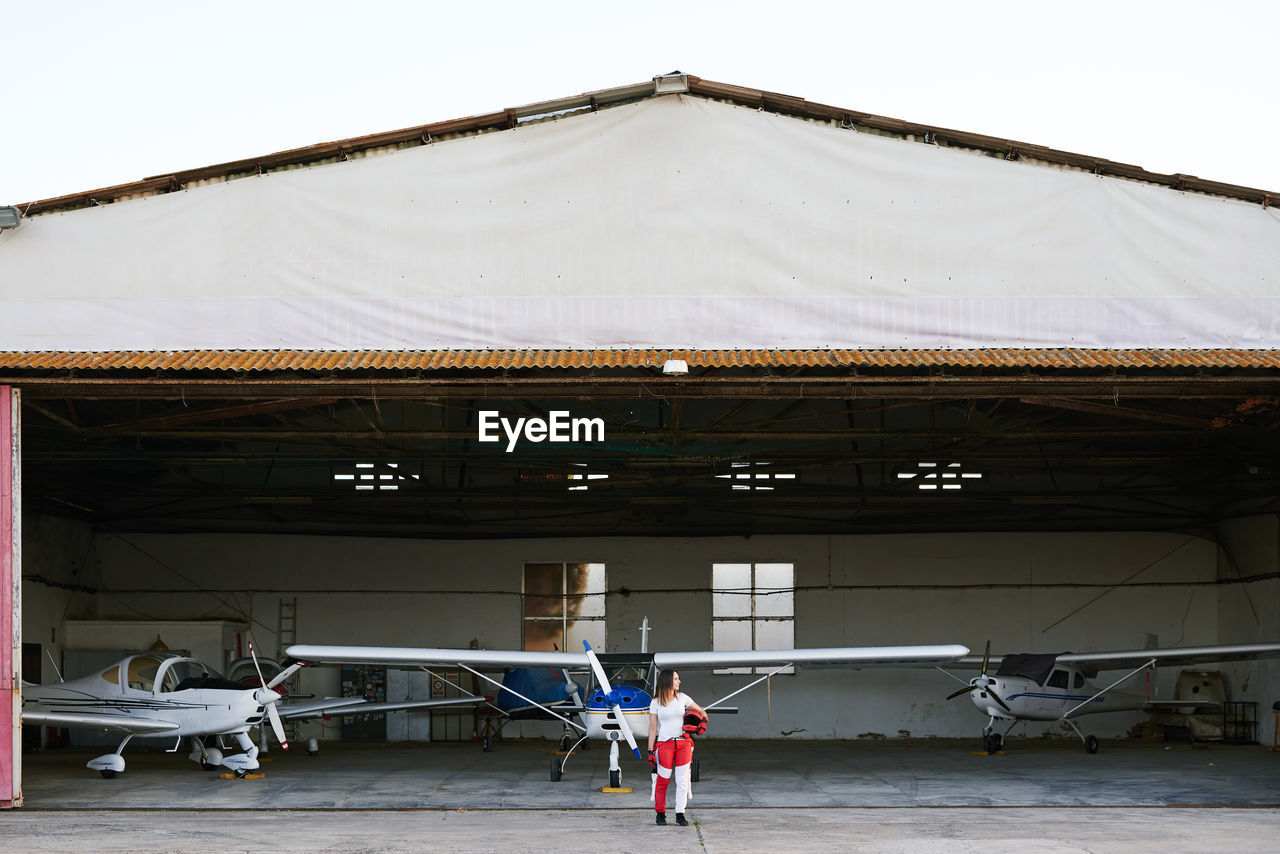 Young female skydiver in a plane hangar surrounded by planes