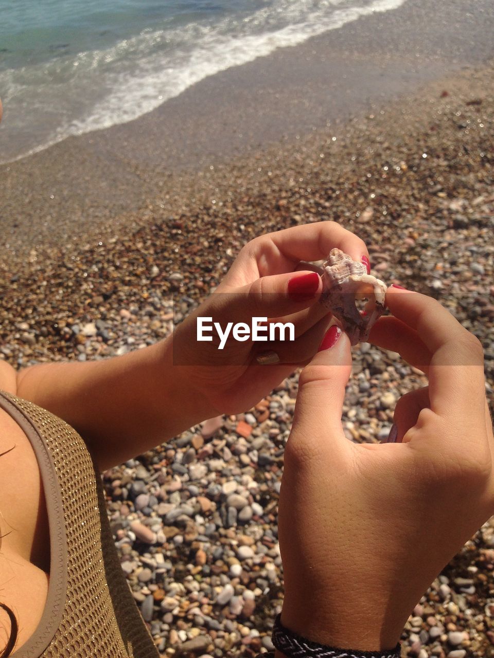 MIDSECTION OF PERSON HOLDING PEBBLES ON BEACH