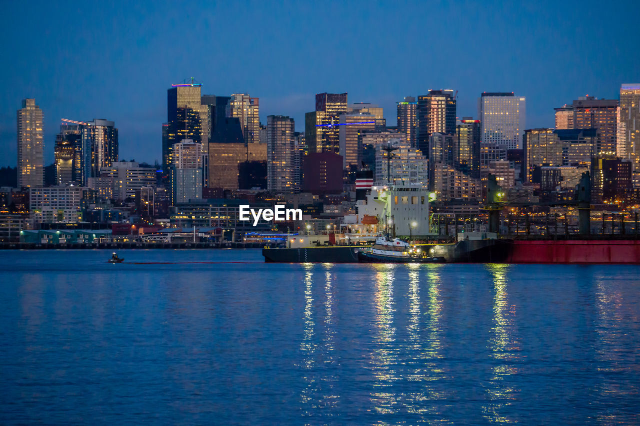 Illuminated buildings by sea against blue sky