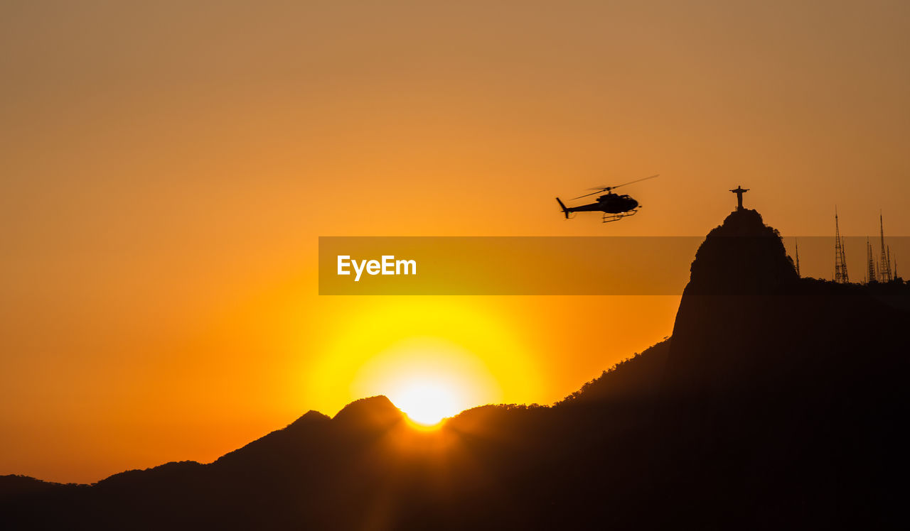 SILHOUETTE OF AIRPLANE FLYING AGAINST ORANGE SKY