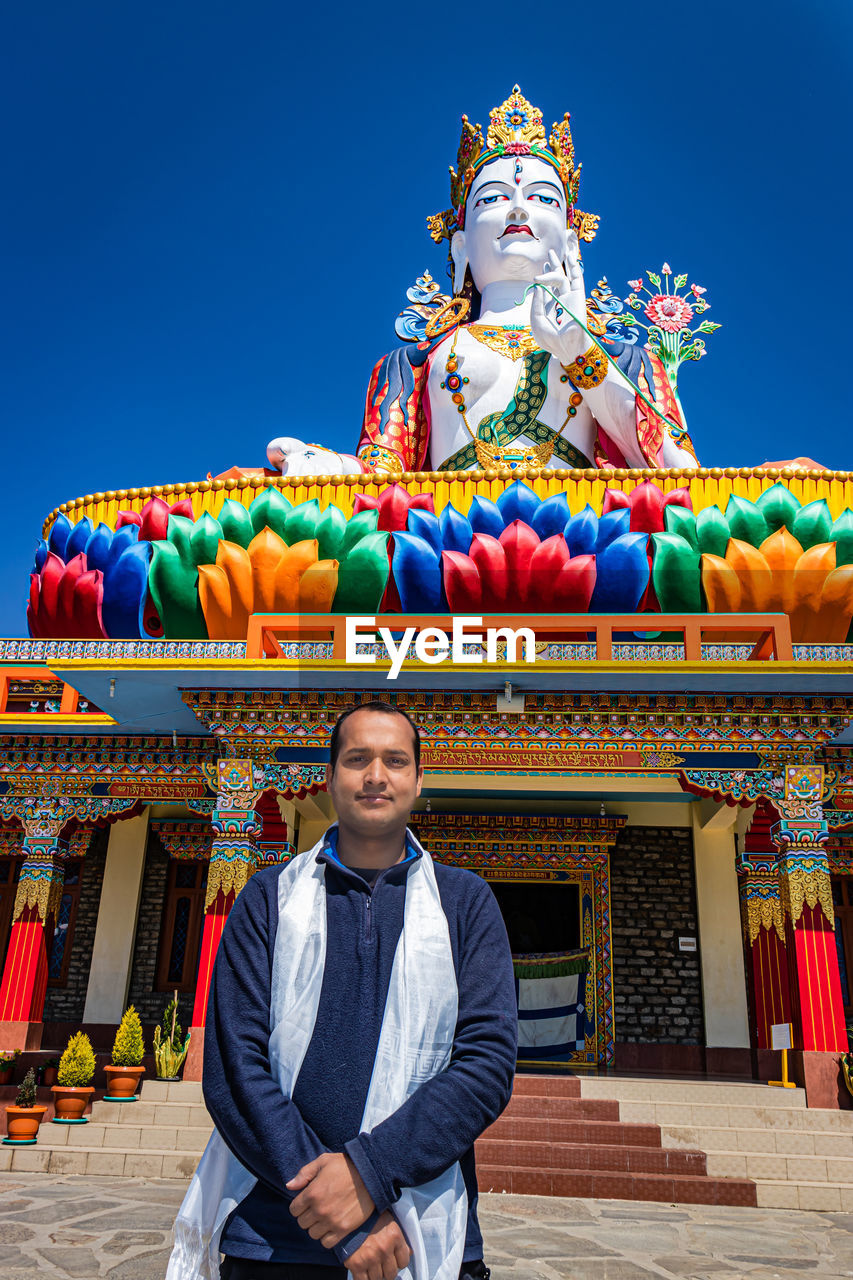Young man praying in front of buddhist colorful goddess statue with blue sky at morning