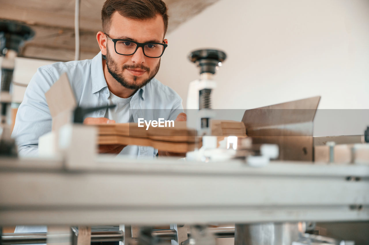 adult, men, occupation, working, one person, indoors, glasses, eyeglasses, business, person, beard, education, business finance and industry, technology, facial hair, concentration, industry, expertise, workshop, science, research, skill, looking, protective eyewear, creativity, portrait, small business, selective focus, examining, place of work, front view, professional occupation, scientist, human face, scientific experiment, laboratory, office, table, equipment