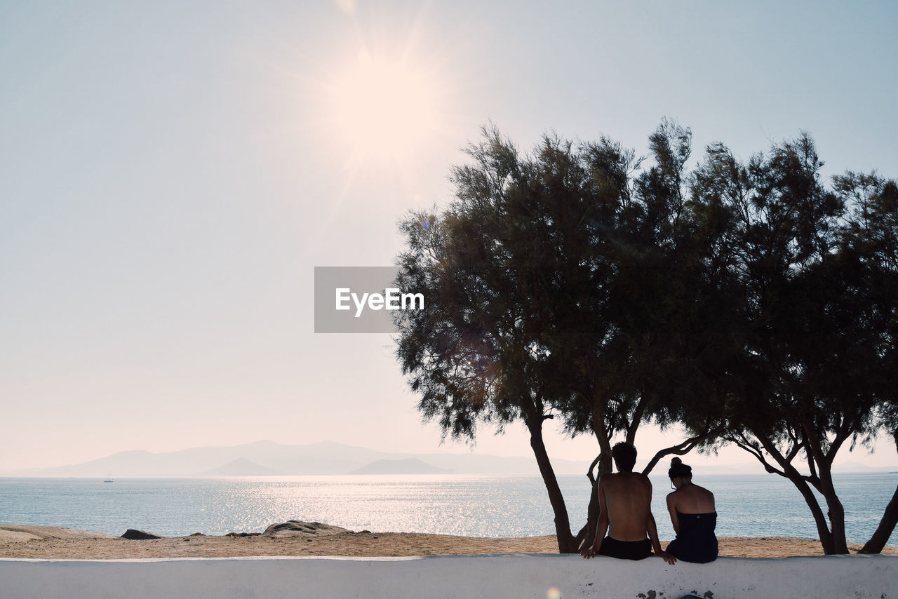 PEOPLE STANDING AT BEACH AGAINST CLEAR SKY