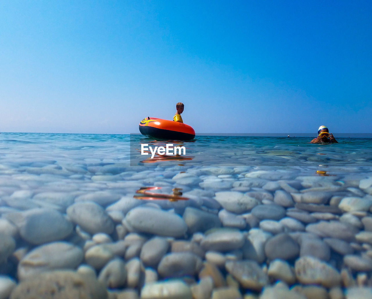 Water surface shot of siblings swimming in sea against clear blue sky during sunny day