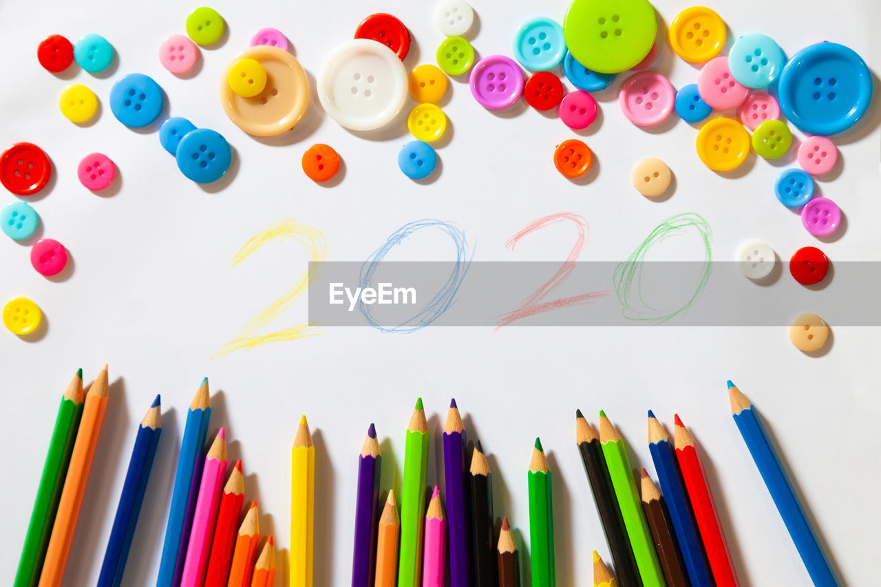 Directly above view of colored pencils with 2020 number and buttons on white table