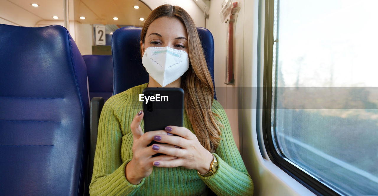 Relaxed train passenger using smartphone app during travel commute wearing protective face mask