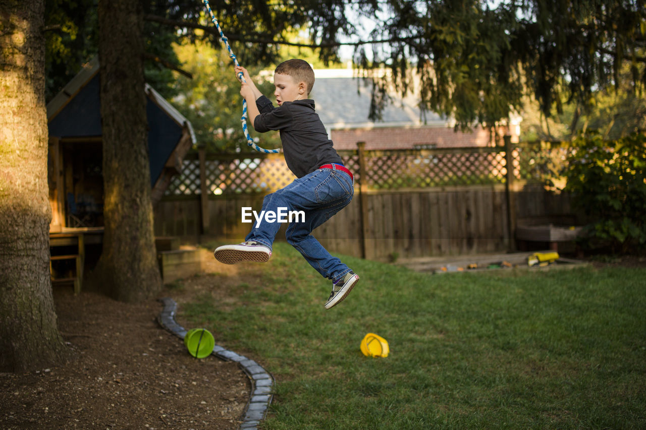 A small boy swings on a rope in his back yard