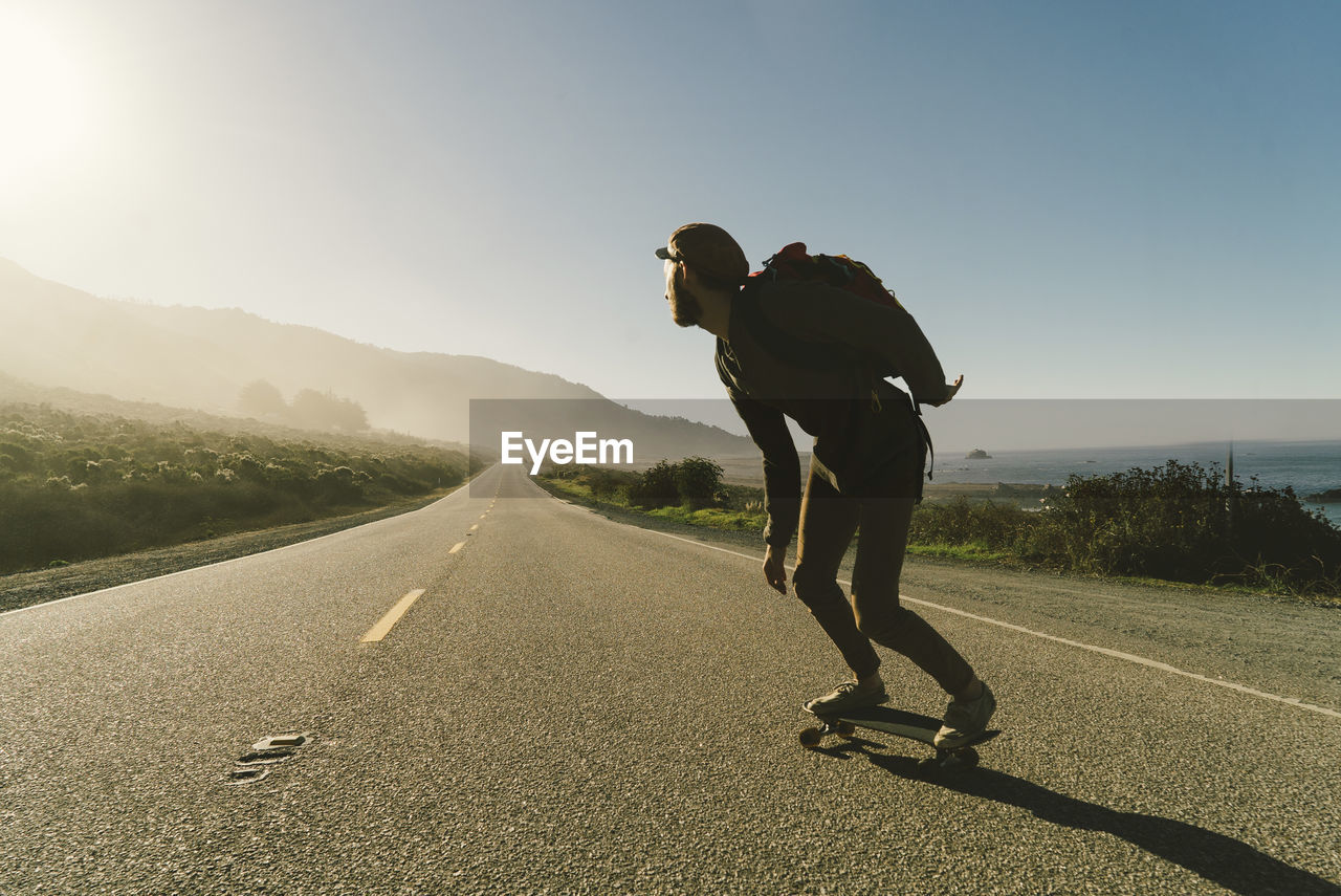 Full length of man skateboarding on country road