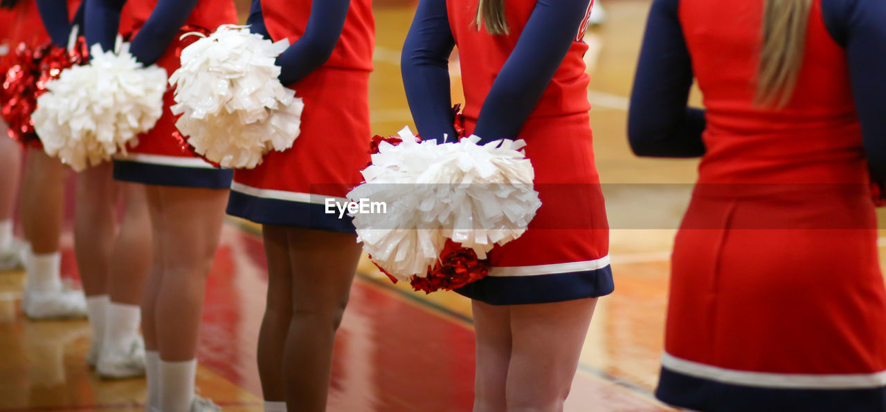 Cheerleader's with their pom poms behind their backs while watching their basketball team.