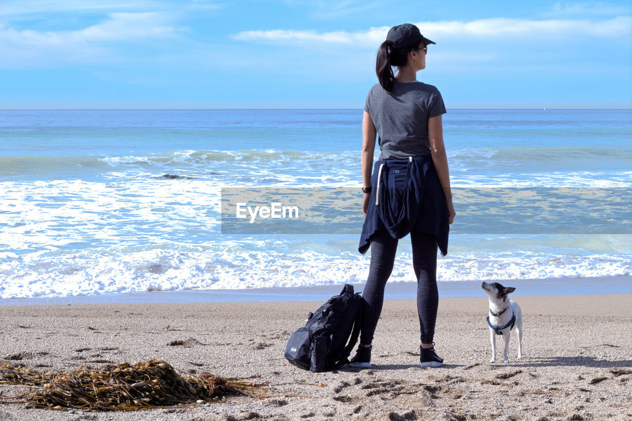 Rear view full length of woman sitting with dog on shore at beach