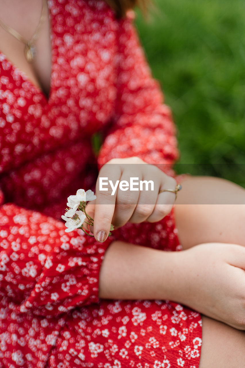 Woman holding a apple blossom flower in her hand wearing a red dress