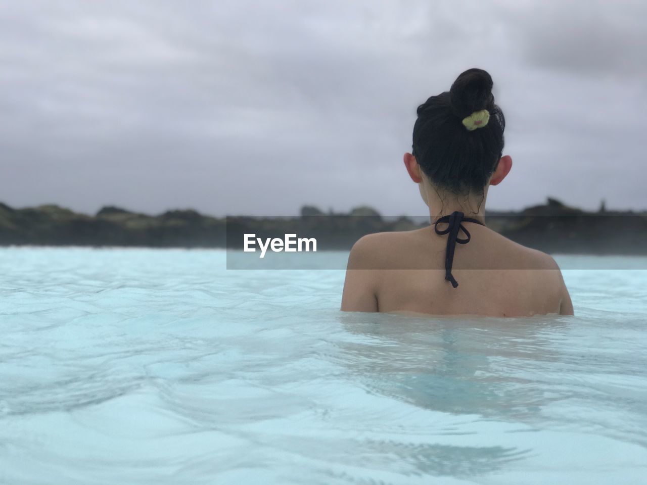Rear view of young woman swimming in sea against cloudy sky