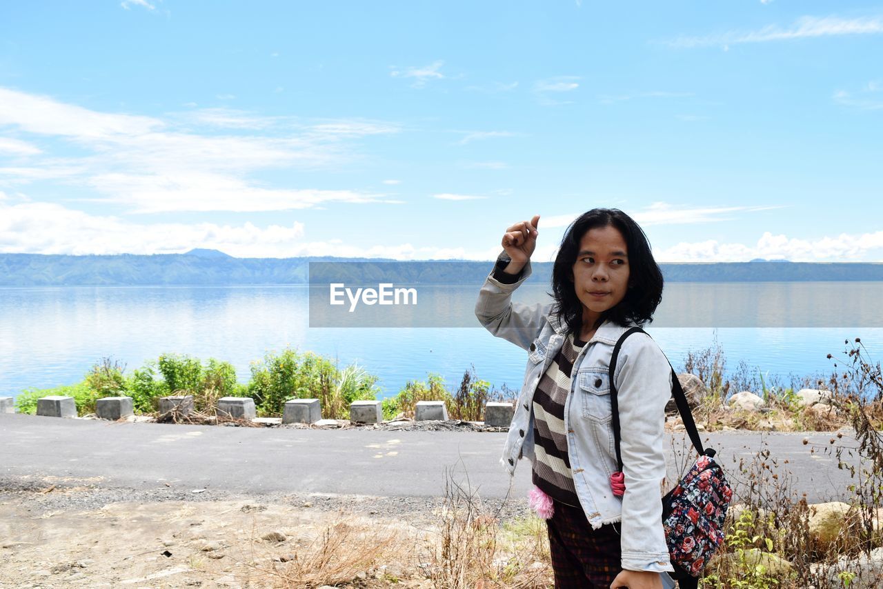 Portrait of smiling young woman standing on shore against sky. lake side and mountains