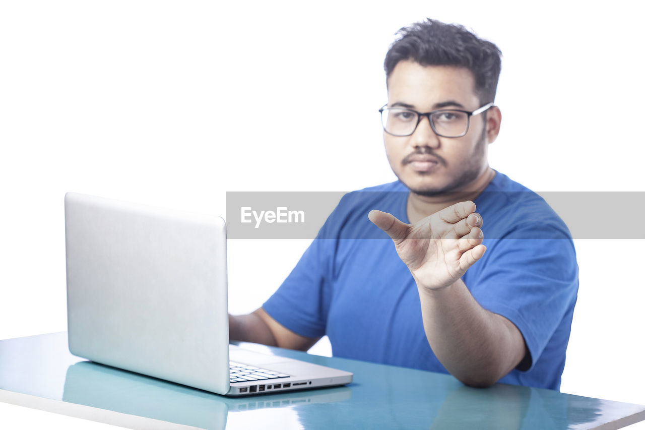technology, computer, eyeglasses, adult, one person, men, business, glasses, laptop, communication, wireless technology, businessman, using laptop, table, office, sitting, indoors, desk, furniture, looking, working, young adult, internet, front view, white-collar worker, business finance and industry, portrait, casual clothing, person, writing, occupation, place of work, computer equipment, copy space, computer network, white background, concentration, button down shirt, relaxation, corporate business, studio shot, e-mail, blue, professional occupation, businesswear, conversation