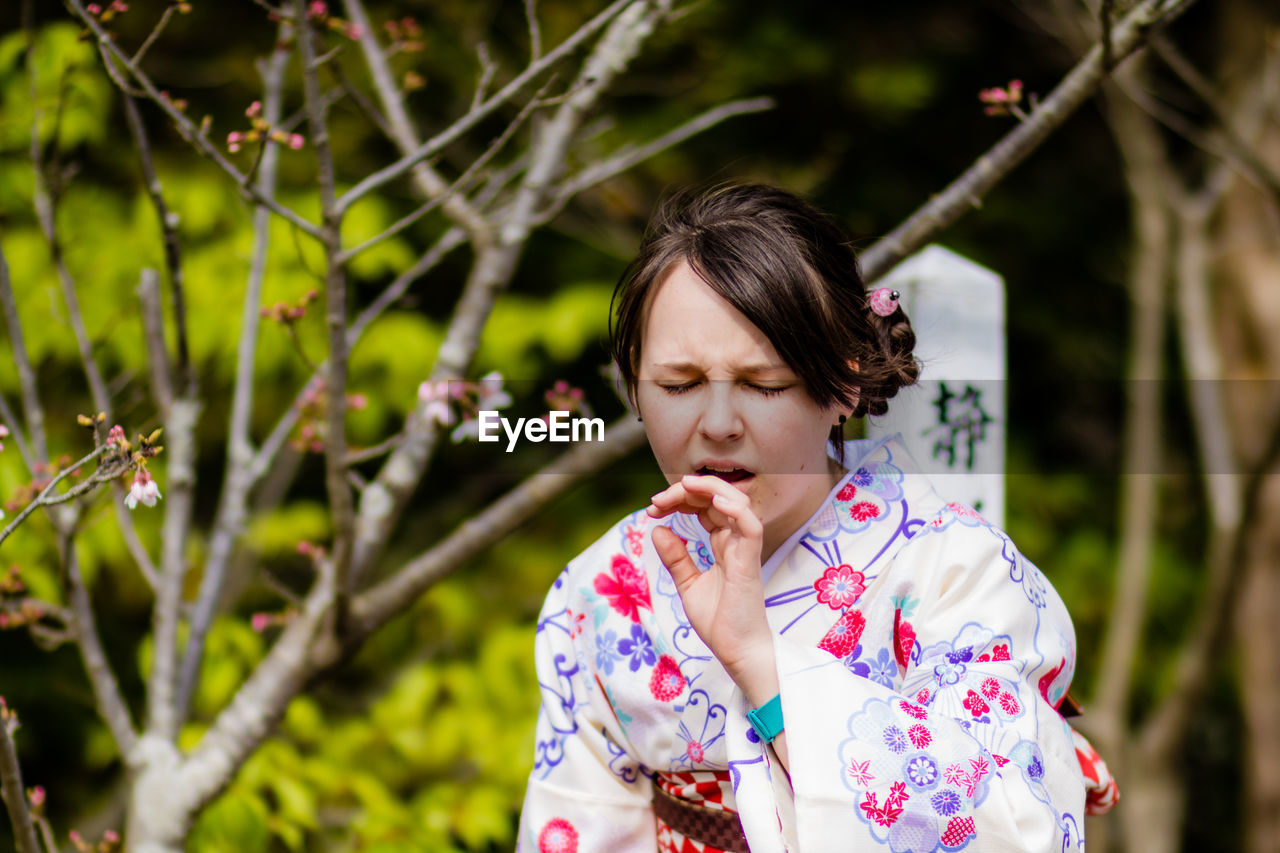 Woman in kimono making face against trees