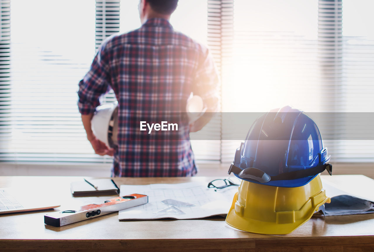 REAR VIEW OF MAN WORKING ON TABLE AT WINDOW