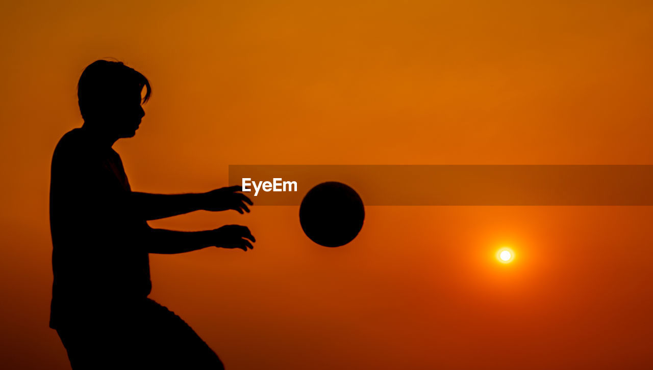 SILHOUETTE MAN PLAYING WITH BALL AGAINST SUNSET SKY