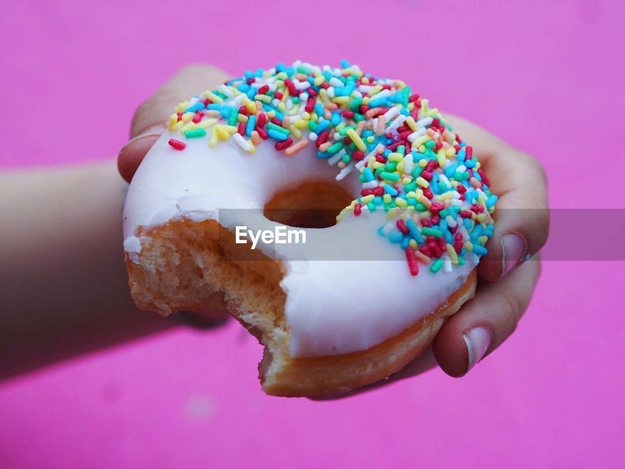 Cropped hand holding donut against pink wall