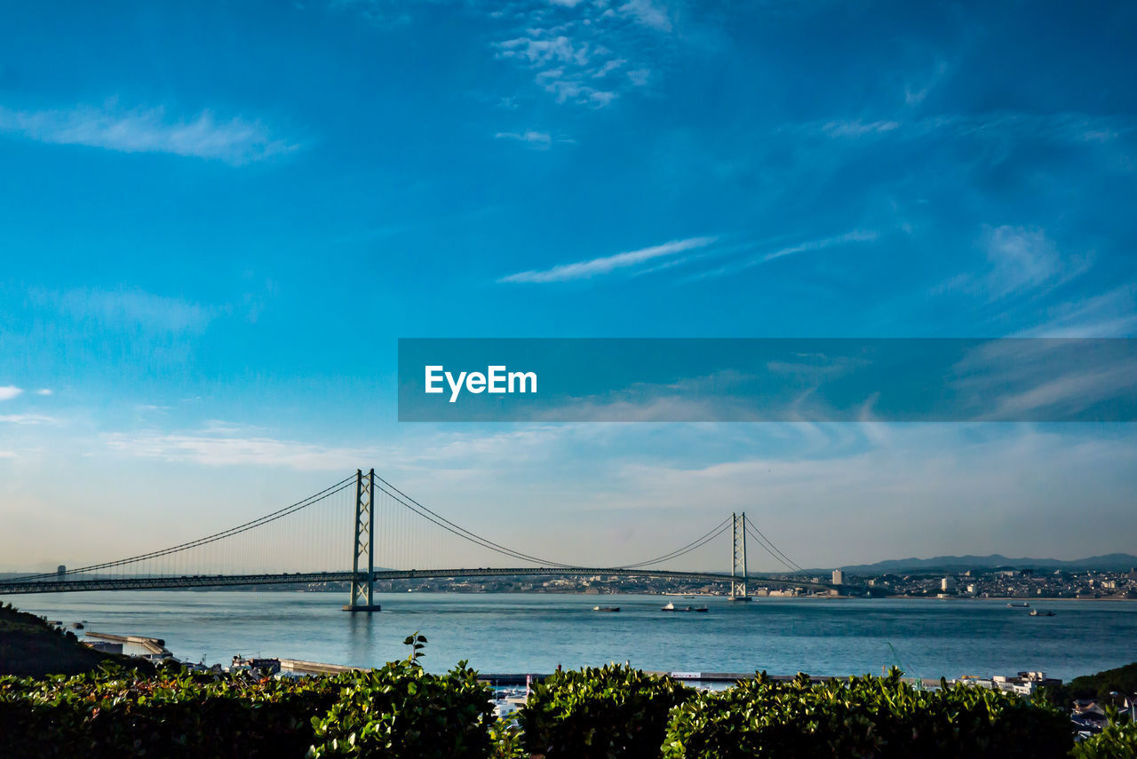 Suspension bridge over sea against cloudy sky