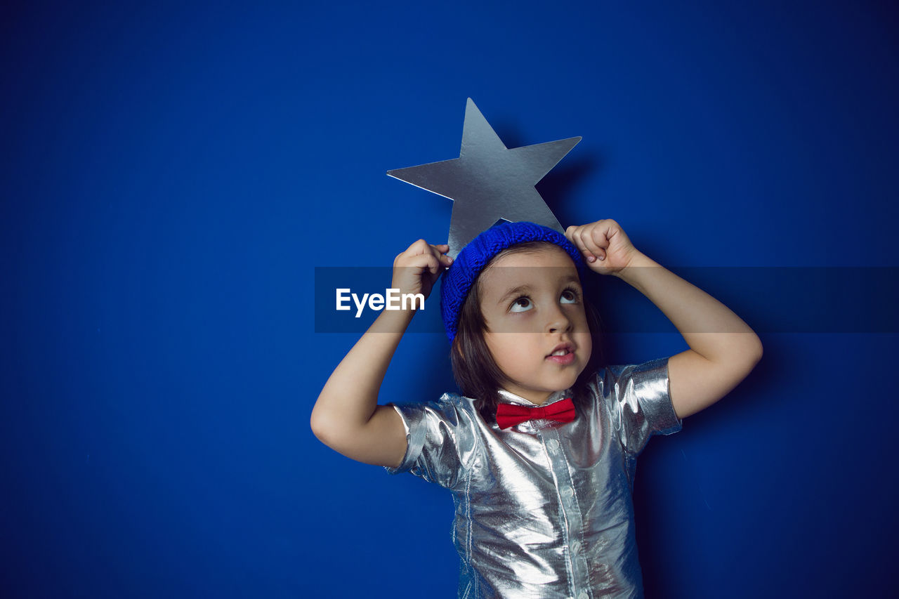 Christmas boy child holding a star in a silver shirt blue hat and red bow tie stands in the studio