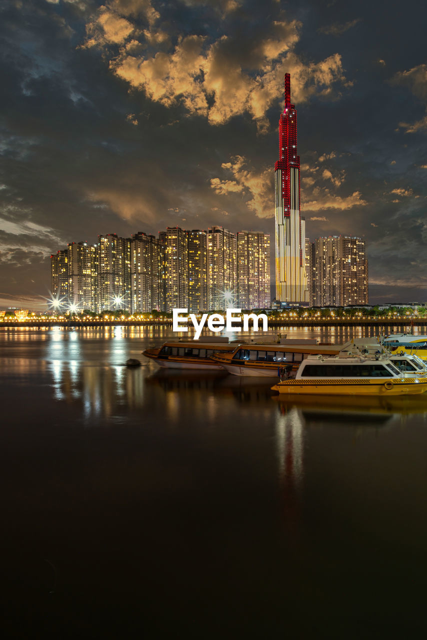 ILLUMINATED MODERN BUILDINGS BY RIVER AGAINST SKY