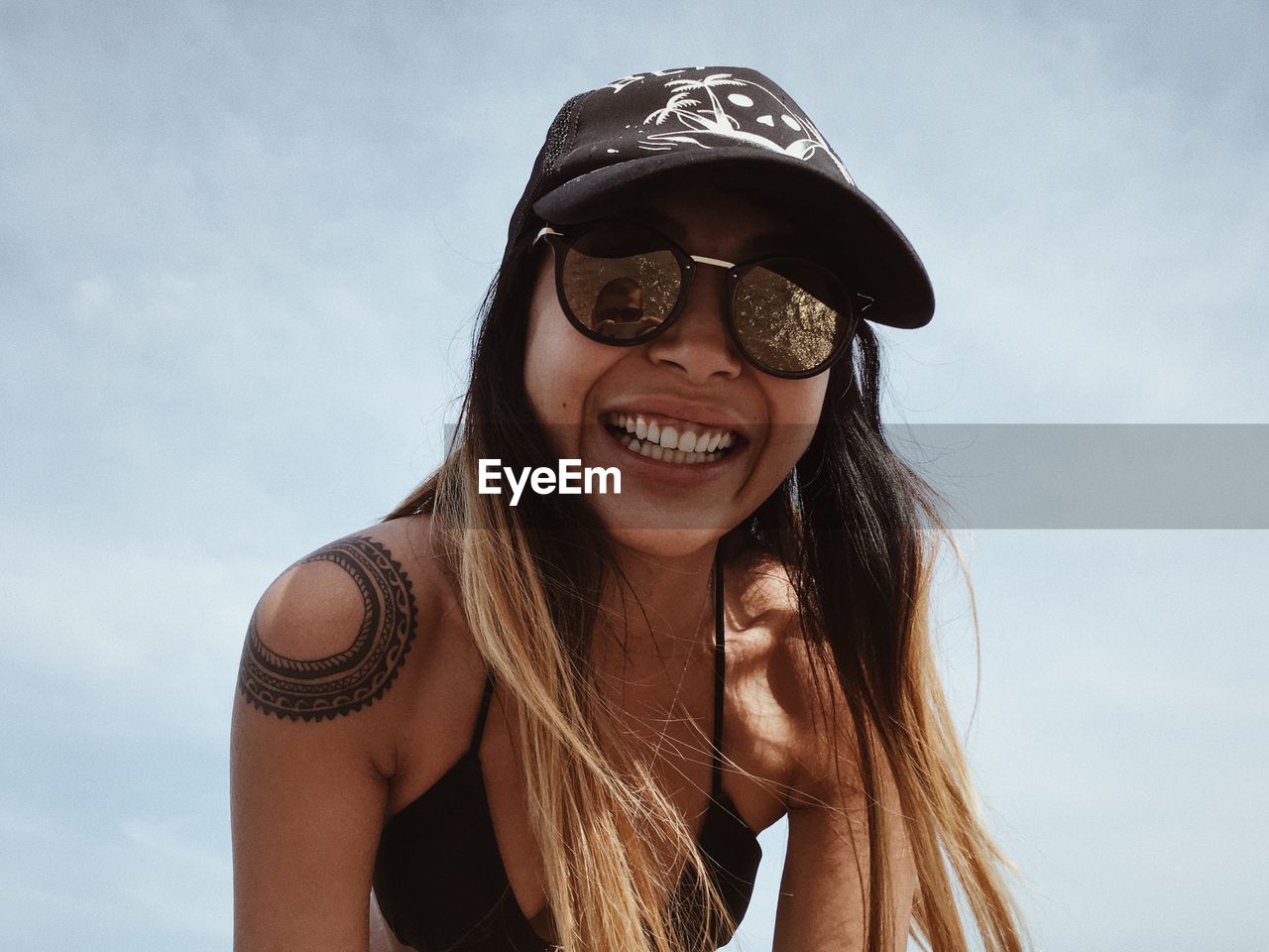 PORTRAIT OF YOUNG WOMAN WITH SUNGLASSES AGAINST SKY