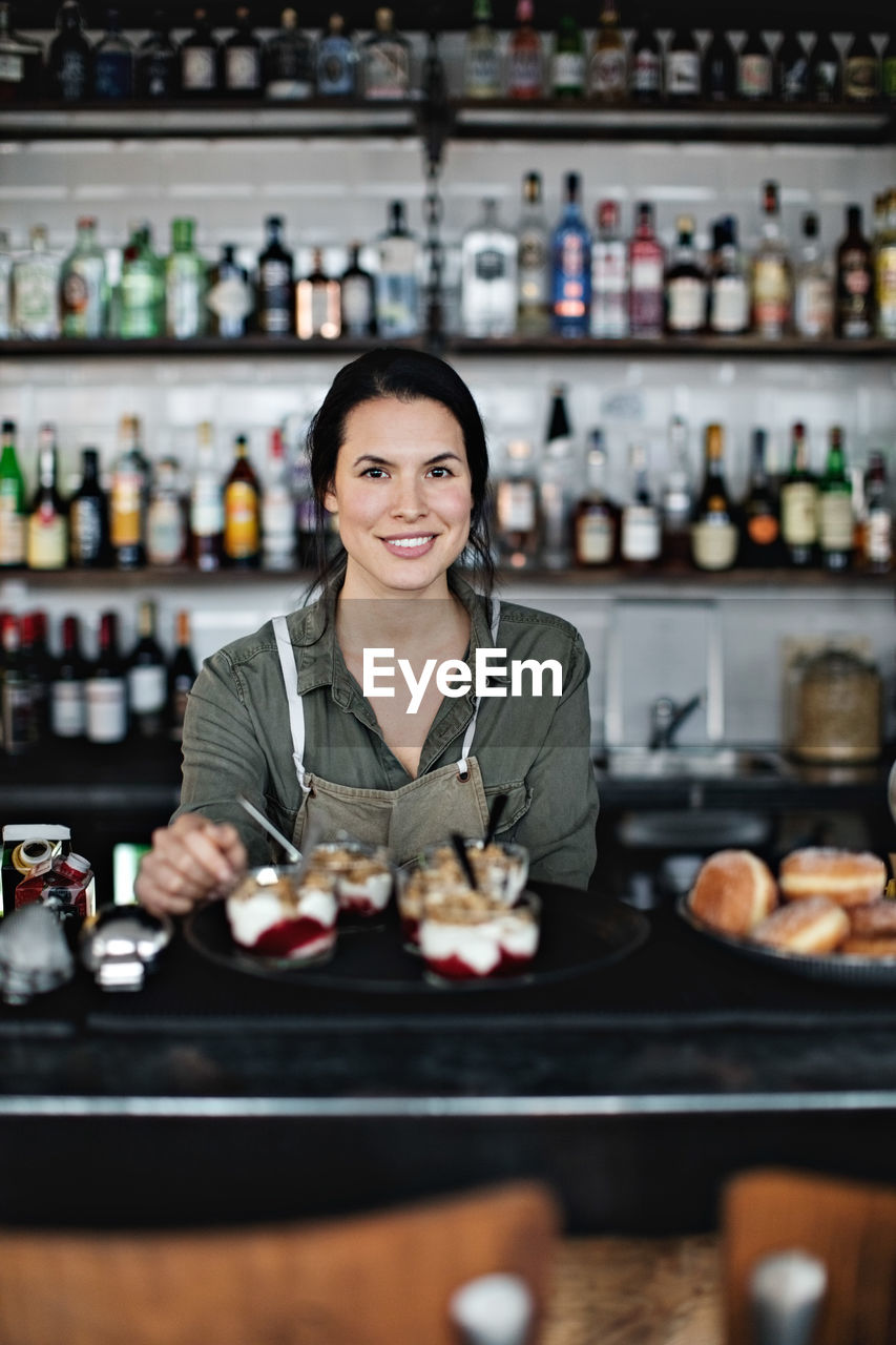 Portrait of smiling female owner with dessert standing at counter