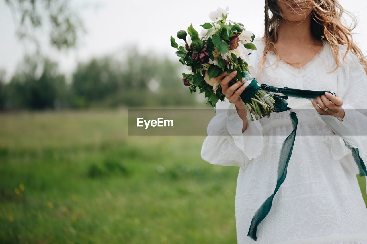 Midsection of woman holding bouquet while standing on field