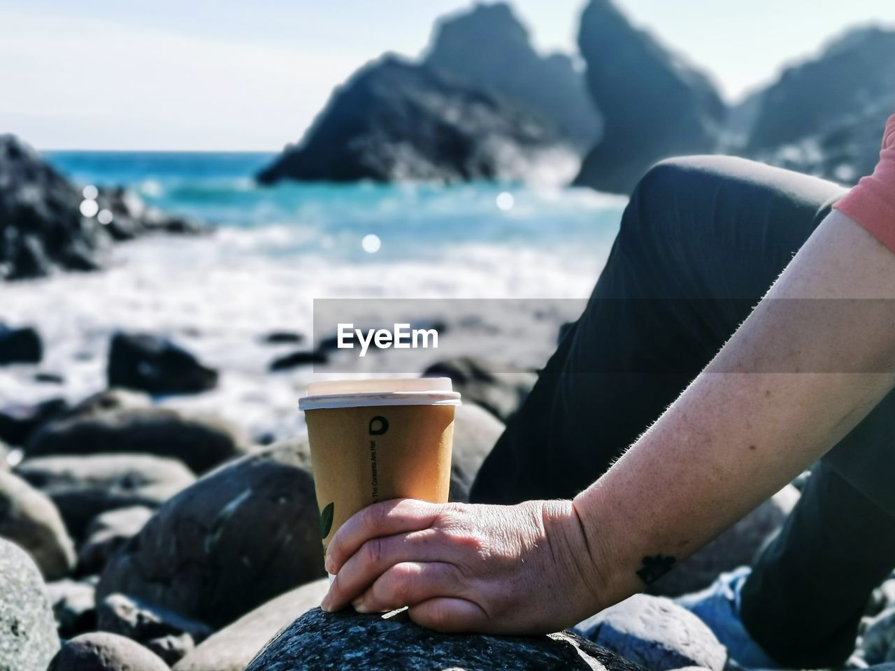 Midsection of woman holding hit drinks cup at beach against sky