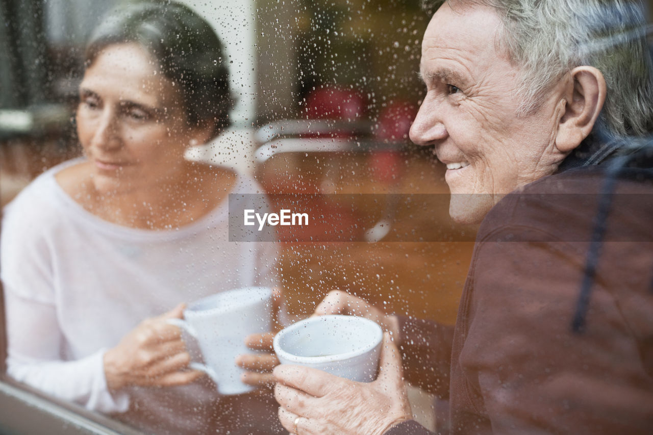 Happy senior couple looking through window at home